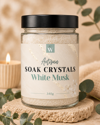 Jar of Artisan Soak Crystals White Musk on a natural stone surface with eucalyptus leaves and a candle in the background.